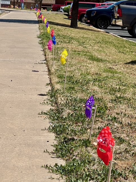 Long row of colorful pinwheels lining a sidewalk near a parking lot