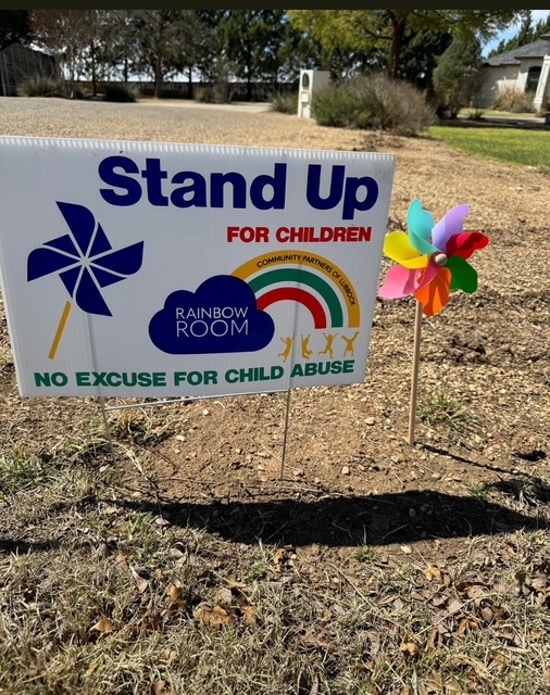 Stand Up For Children yard sign with a colorful pinwheel in a residential yard