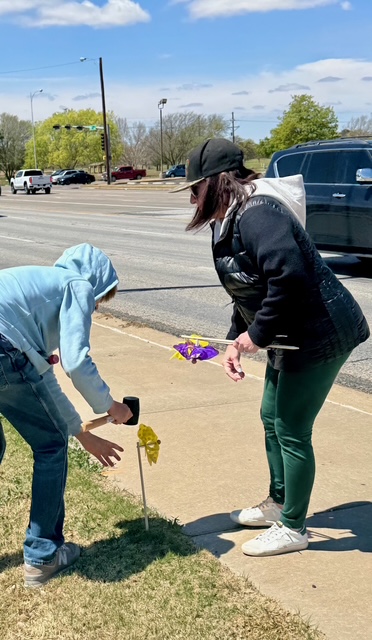 Two volunteers planting a yellow pinwheel near a sidewalk