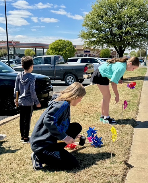 Young volunteers planting colorful pinwheels in the ground on a sunny day
