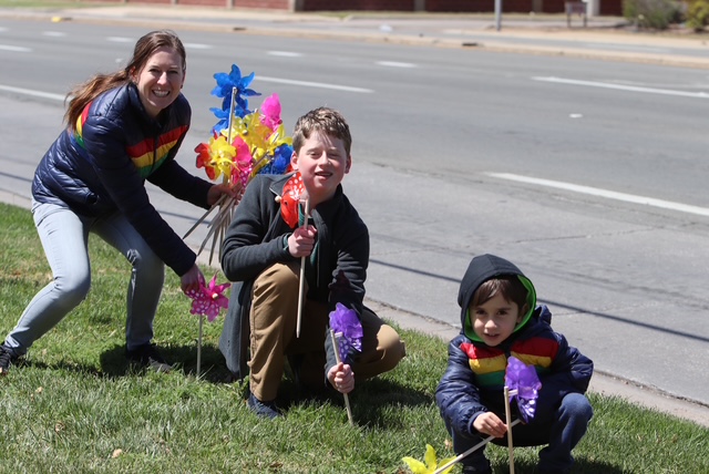 A mother and two children planting colorful pinwheels along a sidewalk